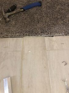 Hammer on carpet edge, wood flooring below. Flooring installation or repair.