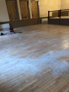 Wooden floor with scattered white powder, near a raised stage and closed doors.