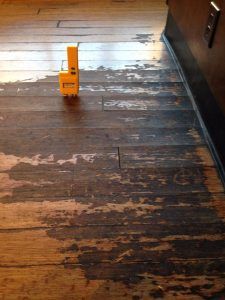 Damaged hardwood floor with dark staining; small yellow tool sits on top.