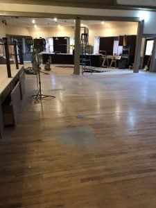 Empty wooden floor of a large room; pillars, some equipment, and a bar area are visible.