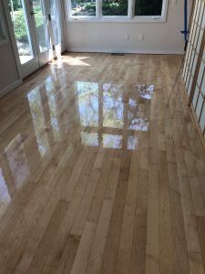 Shiny light-colored hardwood floor reflecting sunlight from windows and doors.