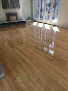 Reflective light on newly refinished hardwood floor in a room with a fireplace and French doors.