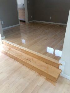 Wooden steps leading up to a room with hardwood flooring and gray walls.