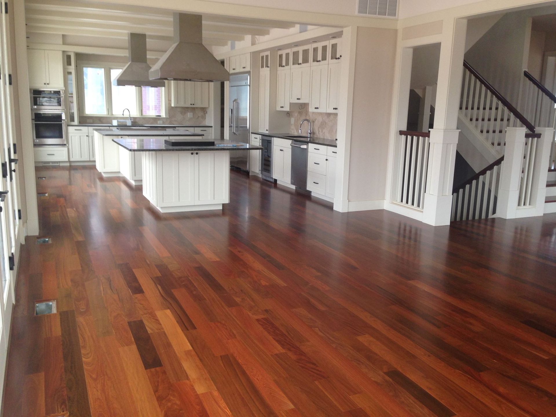 Hardwood floors in a bright kitchen with white cabinets, stainless steel appliances, and a staircase.